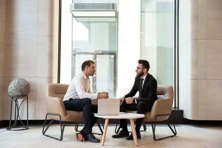 Two men in suits sitting at a table with laptops.